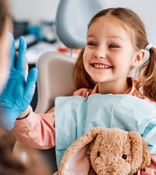 A young girl high-fiving her dentist while holding a plush toy